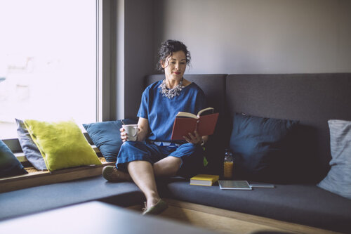 White woman reading on the couch with coffee