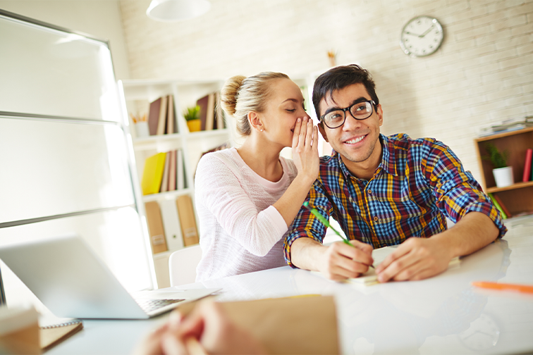 Woman telling secret to man in a bright office